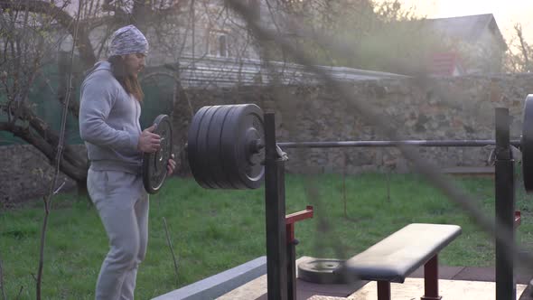 A Man an Athlete in the Early Spring Trains Prepares the Barbell