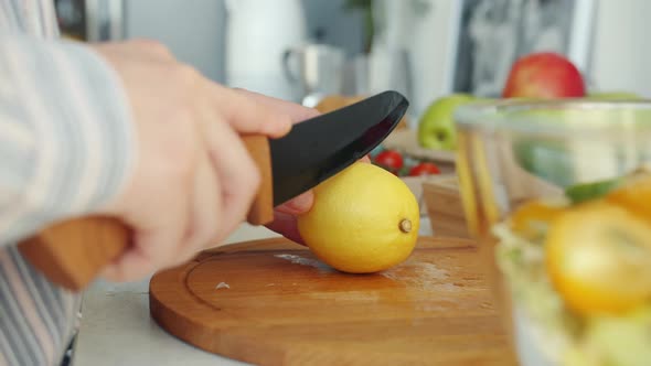 Closeup of Female Hands Cutting Lemon with Knife Cooking Salad in Kitchen