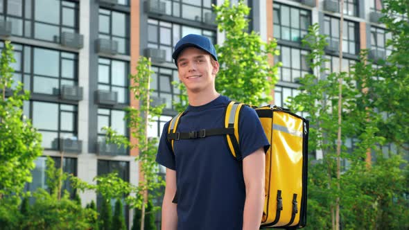 Smiling Man Courier Food Delivery with Backpack Turns Head and Looks Camera