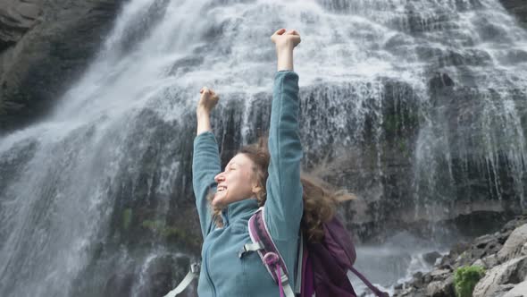 Happy Lady with Hands Up Rejoices Standing Near Waterfall