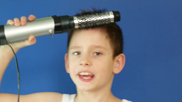Portrait of a caucasian boy 7 years old combing drying hair with a hair dryer.