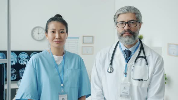 Portrait of Male Physician in White Gown and Female Nurse in Scrubs Standing in Clinic Office