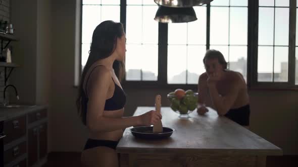 Young Lovers Cooking Breakfast in the Kitchen. Brunette in Bra and Young Man in Underwear Stand Near