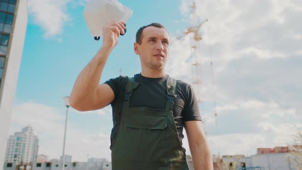 A Worker Work Hard at Construction Site. Tired Male Builder Wipes Sweat From Brow, Standing in Front