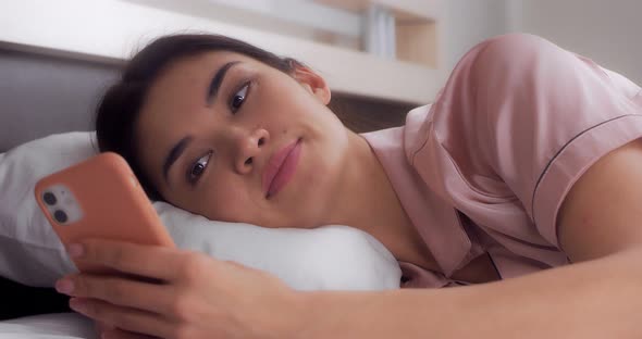 Woman Laughs After Reading a Message on Her Mobile Phone While Lying in Bed