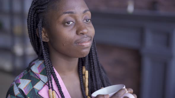 Thoughtful African American Woman with a Cup of Tea or Coffee Looking Away. The Girl with Problem