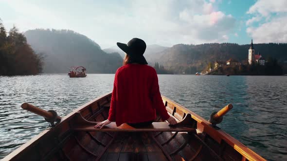 Summer Vacation Ispiration. Romantic Woman in Hat Sitting in Boat on Bled Lake at Hazy Scenic Sunset