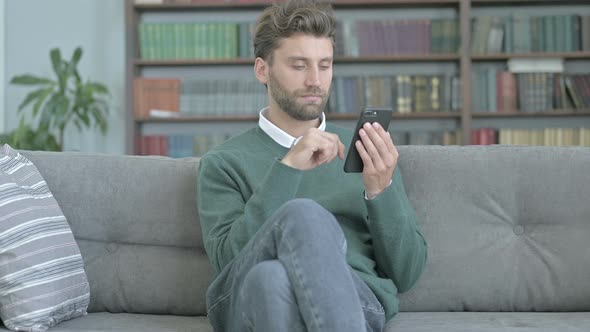 Young Man Sitting on Sofa and Scrolling Through His Smartphone