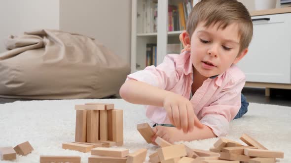 Cute Little Boy Lying on Carpet and Playing with Toy Wooden Blocks