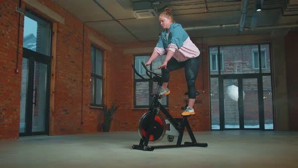 Athletic Girl Performing Aerobic Riding Training Exercises on Cycling Stationary Bike in Foggy Gym