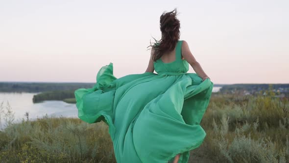 a Young Woman in a Green Long Dress Runs on the Background of a Beautiful Landscape