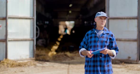 Farmer Gesturing While Writing on Clipboard Against Barn