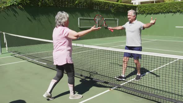 Happy caucasian senior couple embracing over the net at outdoor tennis court after playing a game