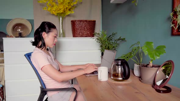 Asian woman reading document on laptop and working at home