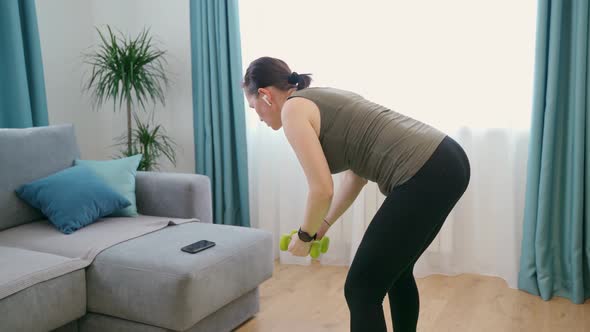 A Woman at Home with Dumbbells in Her Hands Performs Exercises