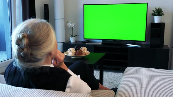 Old Caucasian Woman Watches Television in Living Room and Supports -Green Screen