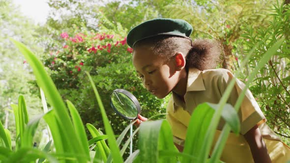 Animation of african american girl in scout costume using magnifier in garden