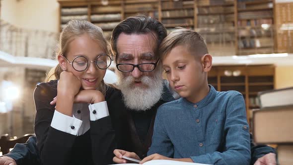 Smiling Grandchildren Sitting Together with their Esteemed Senior Granddad in the Library