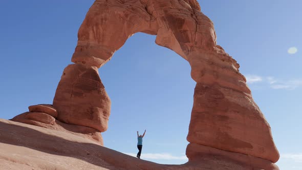 Tourist Raises His Hands Up In A Delicate Arch Of Orange Rock In National Park