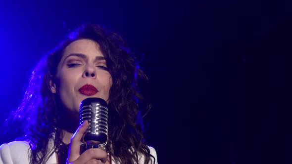 A Stylish Girl Vocalist Sings on Stage in a Vintage Microphone. Dark Studio with Smoke and Neon