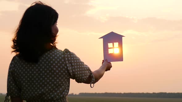 Silhouette Paper Houses During Sunset. The Girl Keeps a Paper House, Dreaming of a Large Cozy House