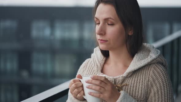 Caucasian Woman Stays on Balcony During Snowfall with Cup of Hot Coffee or Tea