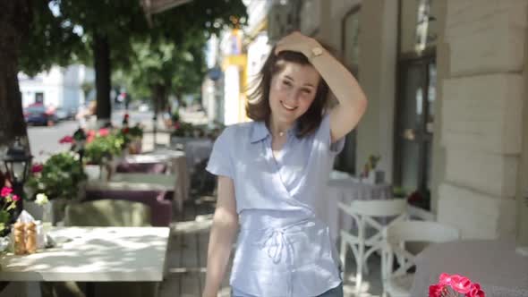 An Enthusiastic Young Woman Walks Along the Landing of a Summer Cafe Between Tables with a Camera in