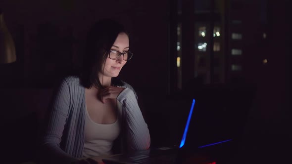 Cute Young Woman Smiling in the Dark Looking at Laptop Screen at Home