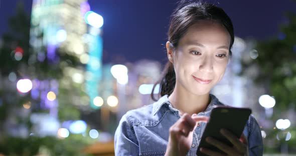 Woman sending text message on cellphone in the city at night 