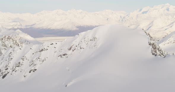 Aerial helicopter shot closeup on rippling glacier, Alaskan mountains in background, tilt down towar