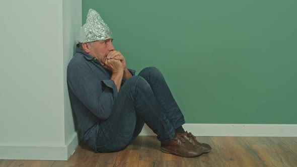 A Paranoid Sitting in a Corner with a Protective Foil Cap on His Head