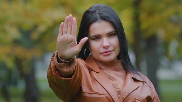 Serious Young Hispanic Girl Standing Outdoors Holds Out Palm Showing Stop Gesture Looking at Camera