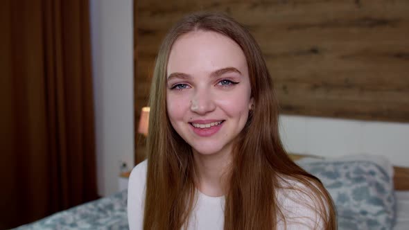 Smiling Pretty Young Woman in Good Mood Looking at Camera Smiles Gently on Bedroom Background