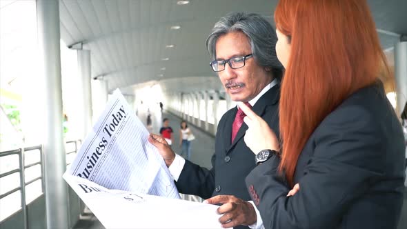 Senior Business Manager and Young Business Woman Talking While Reading Newspaper at Train Platform