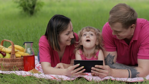 Family Weekend Picnic. Daughter Child Girl with Mother and Father Play Online Games on Tablet