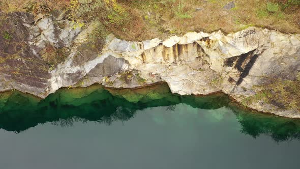 A top down view over a quarry filled with green water. The camera slowly dolly out boom up