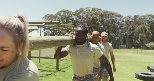 Diverse fit group of soldiers carrying tree log together in the sun at army obstacle course in field alt
