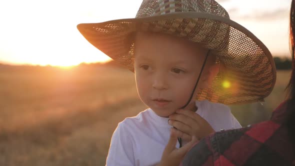 Happy Little Toddler Boy in Hat Having Fun Sitting in Parents Arms in Field in Summer at Sunset