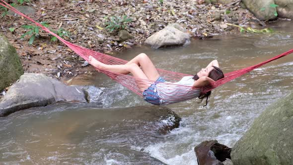 A young asian woman lying and relaxing in hammock in waterfall stream