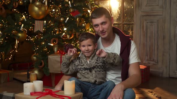 Father and Son Enjoy Christmas Holidays at the Christmas Tree Sitting on the Floor and Looking at