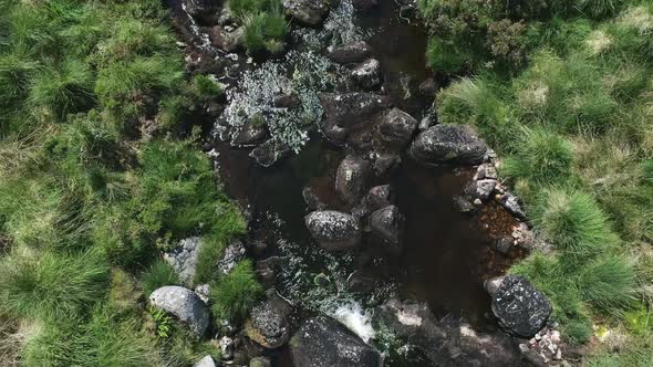 Birdseye close up aerial tracking forward of a rocky river following downstream surrounded by grassy