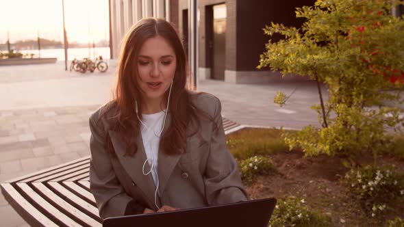 Young attractive business woman sitting outdoor on the bench using laptop