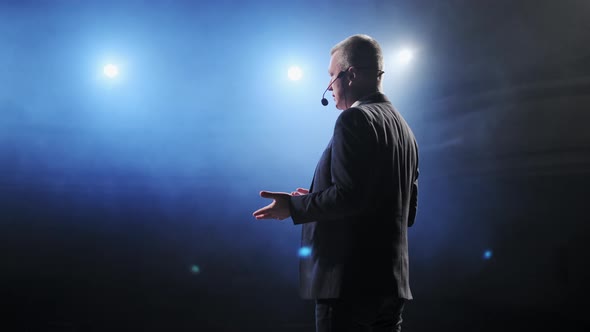 Rear View of Men Speaking Through a Microphone in Dark Conference Hall. Person Says About Marketing