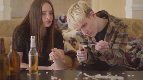 Young Bad Looking Woman and the Man Using Drugs at Home. The Girl Preparing Arm for Injection, Boy