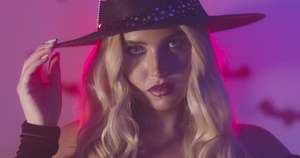 Close Up Beauty Portrait of Gorgeous Blonde Witch, Posing in Neon Lights with Halloween Decorations