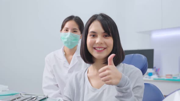 Asian dentist or doctor wearing mask sit behind young beautiful girl patient toothy smile in clinic.