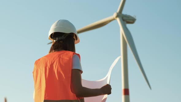 An Engineer of Wind Turbines Holding a Paper Project and Looking at Windmill in the Field