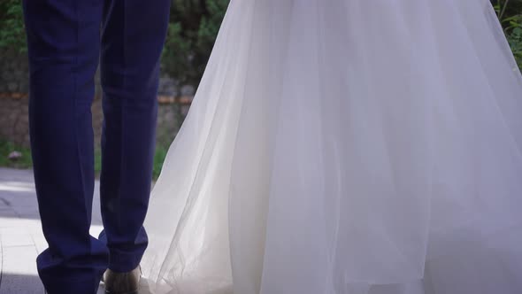 Camera Moves Up As Senior Groom and Bride Holding Hands Walking in Slow Motion Outdoors Talking