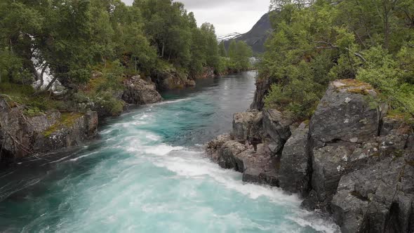 Beautiful blue glacial meltwater river water cascading down mountainside, aerial