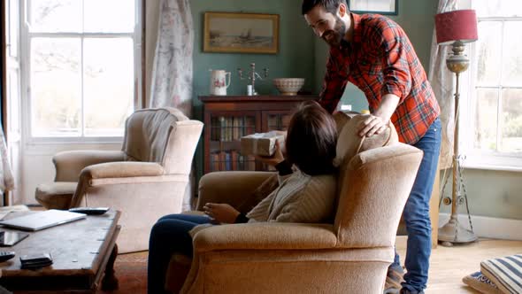 Man surprising woman with a gift in living room